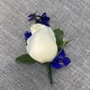 White rose boutonniere with blue accent flowers on gray fabric
