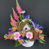 Basket arrangement with pink snapdragons, gerbera daisies, blue irises and a birdhouse centerpiece