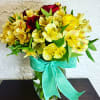 Yellow alstroemeria and red roses in a glass vase with a teal ribbon