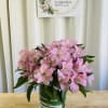 Compact bouquet of pink alstroemeria in a clear glass cylinder vase on a wooden table.