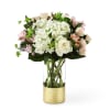 White and blush flowers arranged in a tall glass vase with a gold base