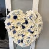 Heart-shaped floral spray with white flowers and blue accents on a stand