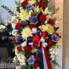Standing floral spray with red, white, and blue flowers and a ribbon bow