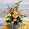 Mixed bouquet in a gray vase with orange roses, yellow spray roses, and pink blooms