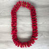 Red carnation lei arranged in an oval shape on a wood surface