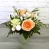 Peach roses and white flowers arranged in a green mug vase