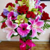Bouquet of pink lilies, red roses, and purple flowers in a glass vase