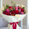 Bouquet of red and pink roses wrapped in white paper with a magenta ribbon