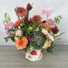 Mixed bouquet in a white mushroom vase with pink, peach, and burgundy blooms