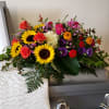 Bright mixed flower spray on a casket with sunflowers, roses, and purple blooms