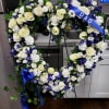 Heart-shaped floral wreath with white roses and blue flowers on a stand