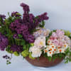 A concrete pot filled with lush lilacs, peonies, roses, viburnums, and narcissus.