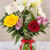 Mixed bouquet of roses and lilies in a glass vase with a red ribbon