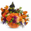 Orange floral arrangement in a pumpkin container with a haunted house pick