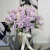 Lavender roses arranged in a vase with pale decorative leaves.