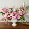 Pink floral arrangement in a white pedestal vase on a wooden cabinet
