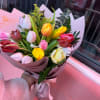 Handheld bouquet of multicolored tulips wrapped in pink paper