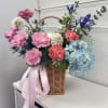 Basket arrangement of pink, blue, and white flowers with a pink ribbon