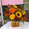 Orange and yellow roses with sunflowers in an amber vase