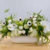 White floral arrangement in a low rectangular vase with green accents