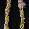 Floral lei with pink buds, yellow flowers, and white beads on a black background
