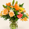 Orange lilies, peach roses, and yellow flowers in a clear glass vase