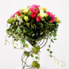 Pink and yellow rose arrangement in a glass vase with trailing ivy