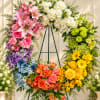 Large rainbow floral wreath on an easel with mixed blooms in pink, white, blue, orange, and yellow.