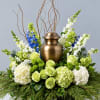 Green and white floral arrangement around a bronze urn with blue accents
