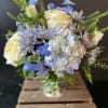Bouquet of cream roses, blue flowers, and lavender blooms in a glass vase