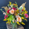 Mixed bouquet of peach roses, pink blooms, and yellow filler in a glass vase