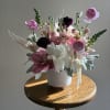 Pink and white floral arrangement in a white vase on a wooden table.