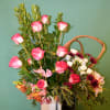 Pink roses and mixed flowers arranged in a white vase with a wicker handle