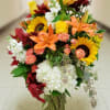 Large mixed bouquet with sunflowers, lilies, roses, and white hydrangeas in a glass vase