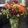 Mixed bouquet of orange roses, magenta carnations, and yellow blooms in a glass vase