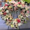 Heart-shaped standing wreath of white, pink, and cream flowers with roses, lilies, and carnations on a black easel.