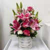 Pink lilies and roses arranged in a white basket vase with pearl trim