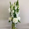 Tall white hydrangeas and snapdragons arranged in a clear glass vase on a small wooden stand