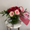 Short arrangement of red and pink roses with greenery in a glass vase, accented with a red and pink bow.