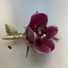 Magenta orchid corsage with small pink blooms and gold glitter accents on a white background