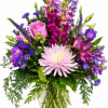 Mixed bouquet of pink, purple, and blue flowers in a clear glass vase