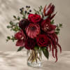Deep red bouquet in a clear glass vase with roses and tropical blooms