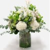 White orchids and hydrangeas in a glass vase with green accents