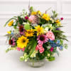 Mixed bouquet of yellow, pink, purple, and white flowers in a clear glass vase