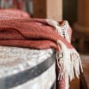 Folded red patterned throw blanket with white fringe draped over a surface