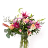 Mixed bouquet of pink lilies, peach roses, and pastel blooms in a clear textured glass vase