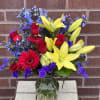 Bouquet of red roses, yellow lilies, and blue flowers in a glass vase
