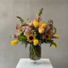 Mixed bouquet of tulips, roses, sunflowers, and pink blooms in a glass vase