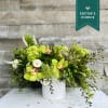 Green floral arrangement in a white vase with orchids and succulents