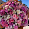 Large bouquet of pink, purple, and white roses wrapped in pastel paper